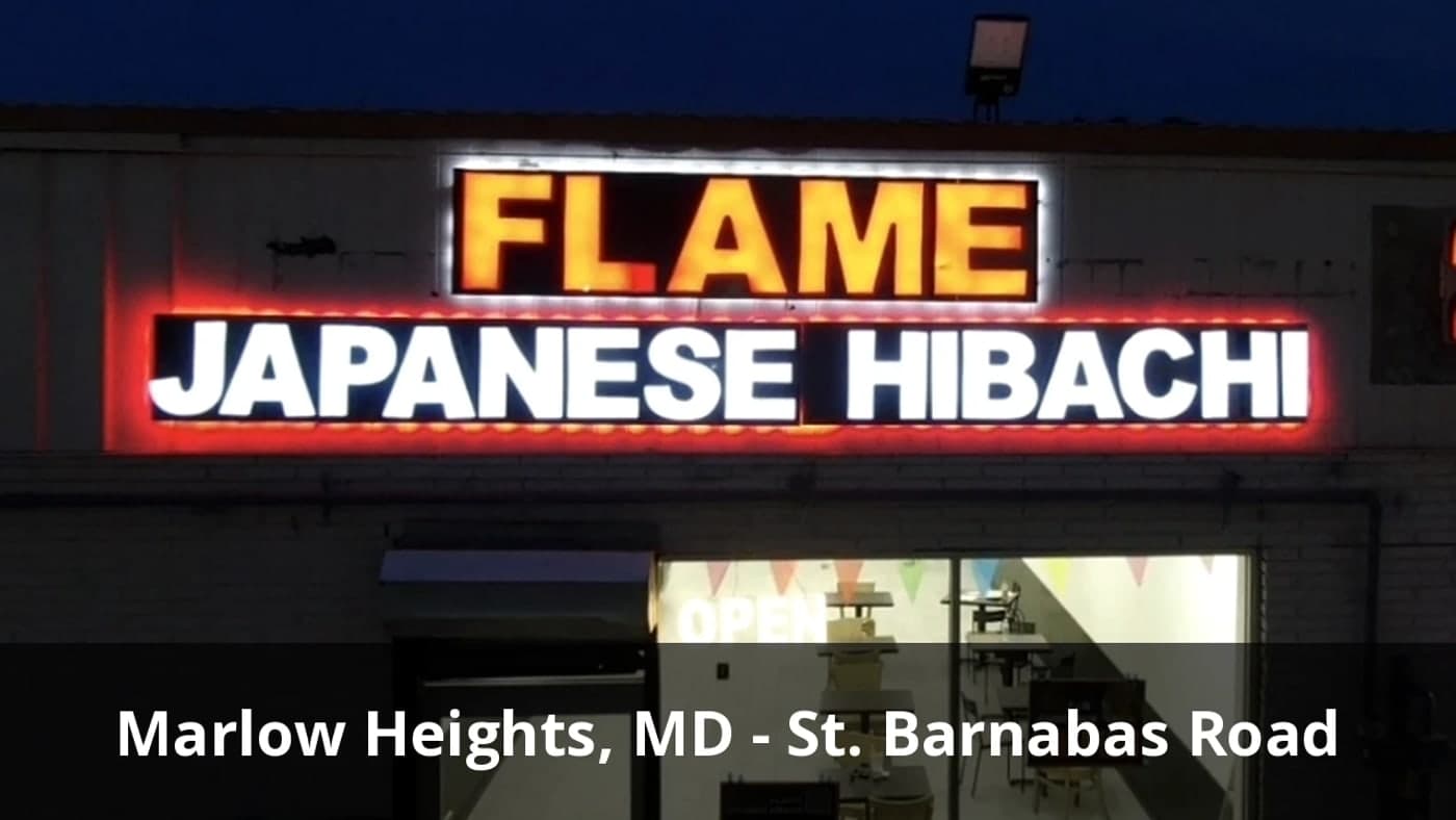 Illuminated storefront of Flame Japanese Hibachi on St Barnabas Road in Marlow Heights, Maryland, open in the evening